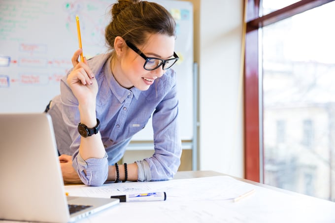 Happy young woman in glasses standing near the window in office and working on a maintenance plan